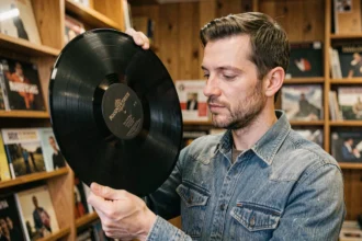 Homme tenant un vinyle 33 tours de 30 cm dans un magasin de disques indépendant, examinant les sillons de près